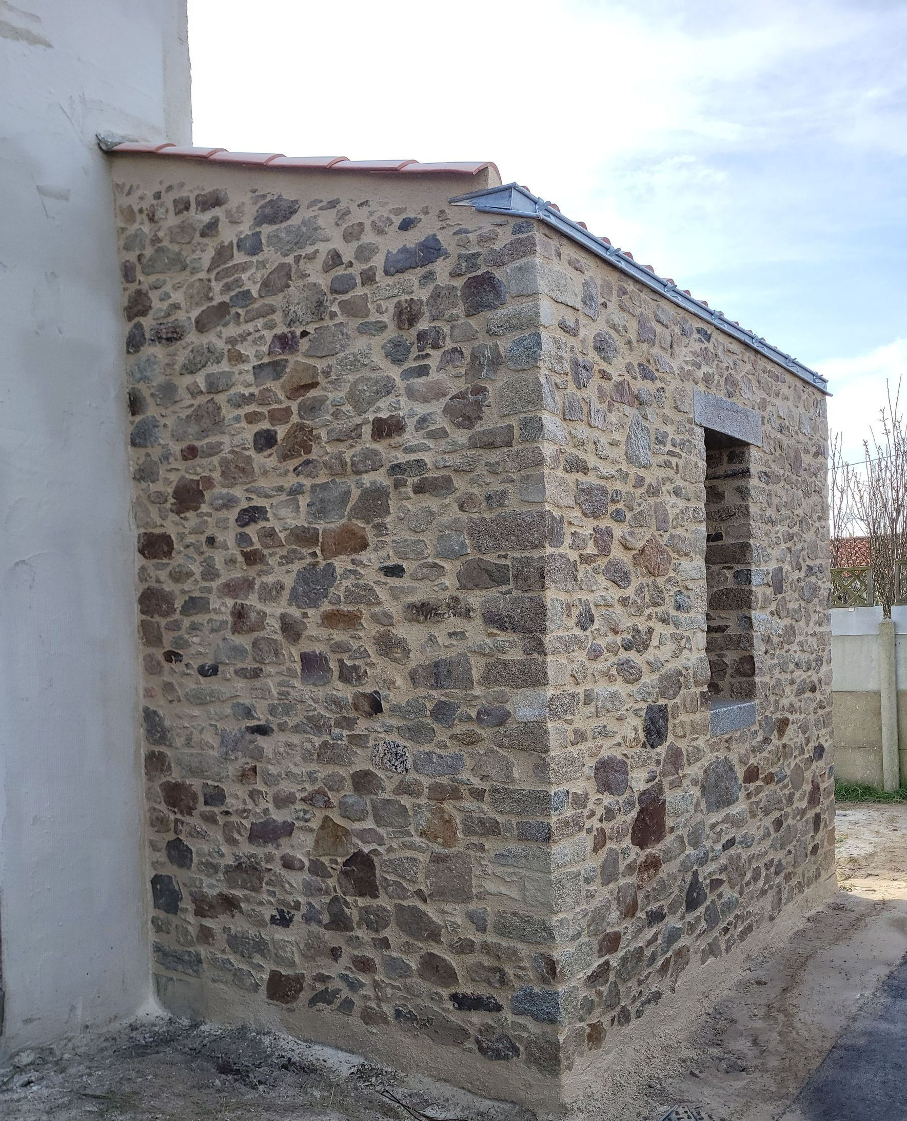 Bâtiment en pierre avec une petite fenêtre, un toit et un mur extérieur clair.
