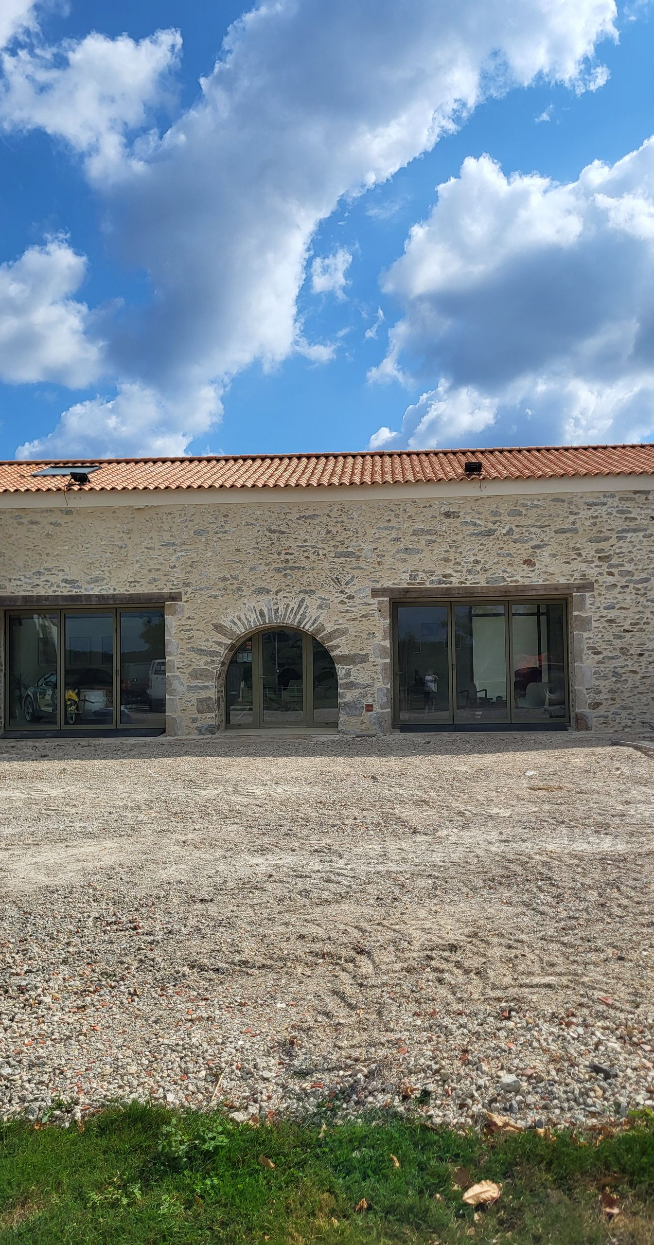 Bâtiment en pierre avec fenêtre cintrée et fenêtres rectangulaires sous un ciel bleu nuageux.