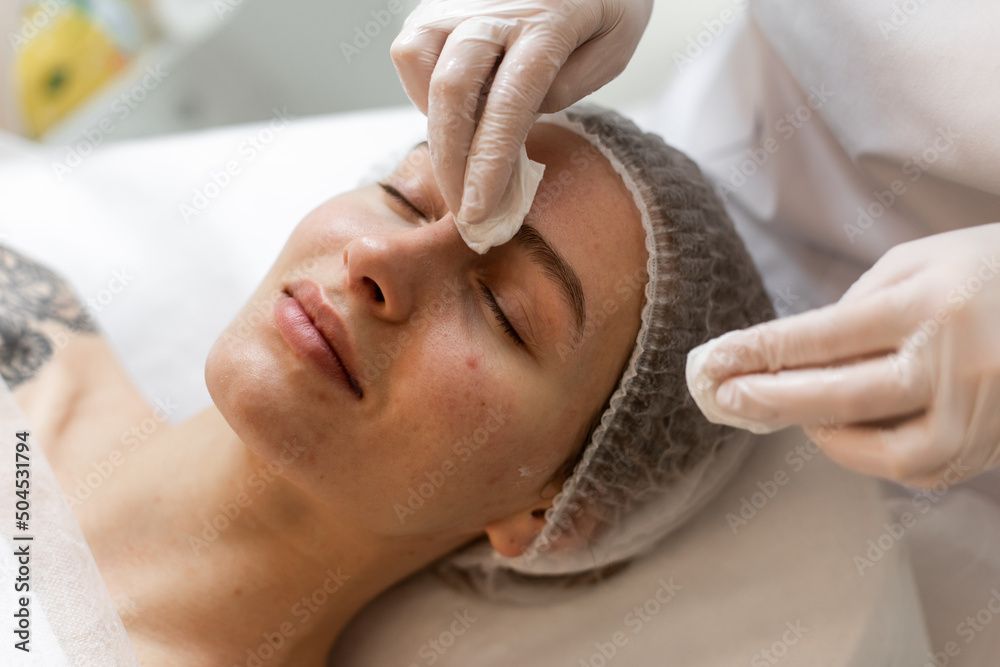 Gesichtsbehandlung im Gange, wobei behandschuhte Hände das Produkt auf das Gesicht eines Kunden auftragen.