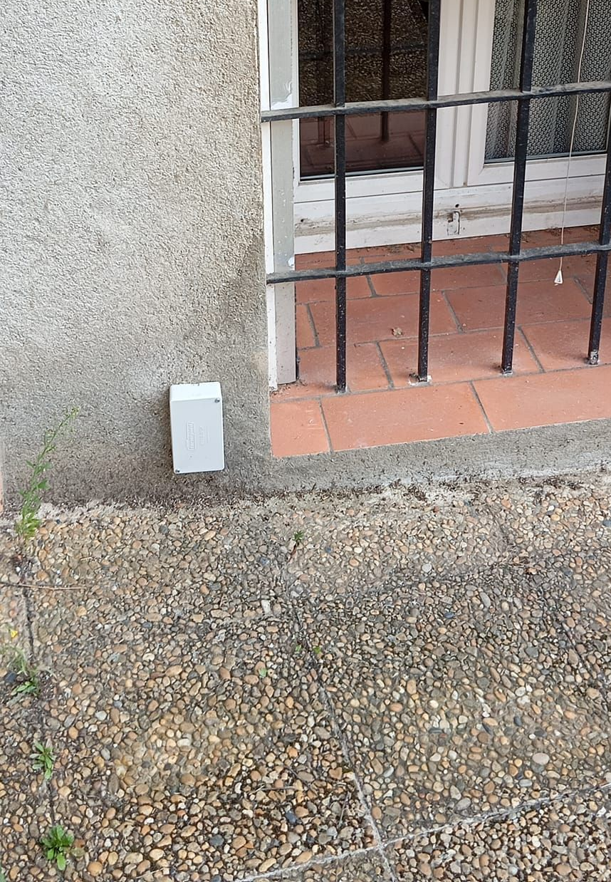 Un piège à termites blanc à côté d'une fenêtre.