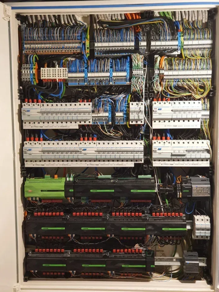 Elektrisches Bedienfeld mit zahlreichen Kabeln, Schaltkreisen und Komponenten. Meistens schwarz, weiß, grün und blau.