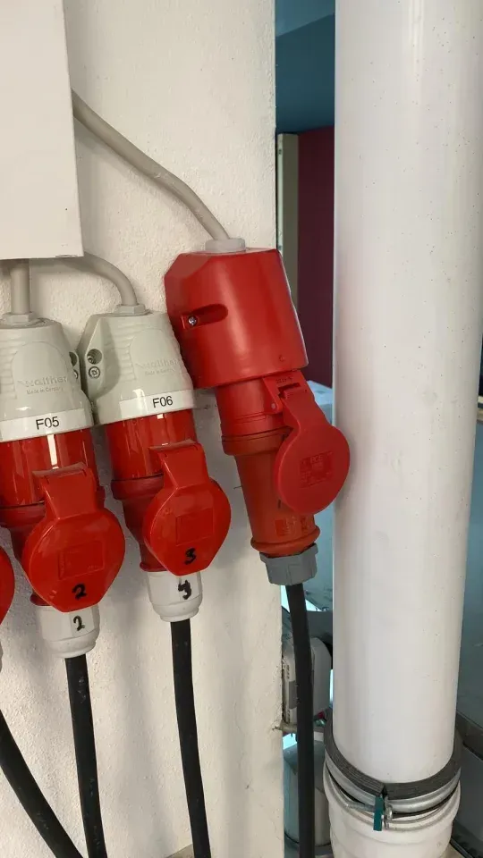 Rote und weiße Industriestecker sind an einer Wand neben einem weißen Rohr montiert.
