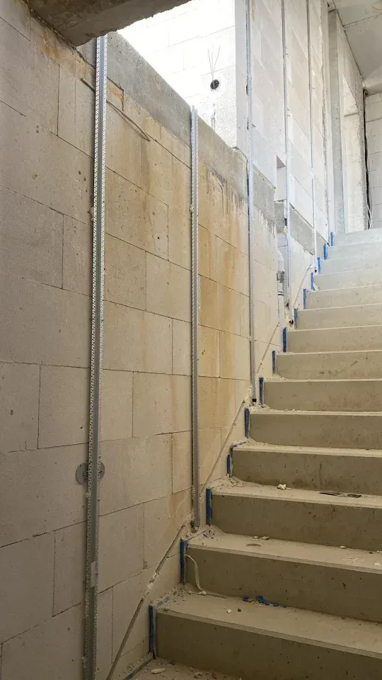 Im Bau befindliche Treppe mit Betonstufen und Metallbolzen vor einer Blockwand.