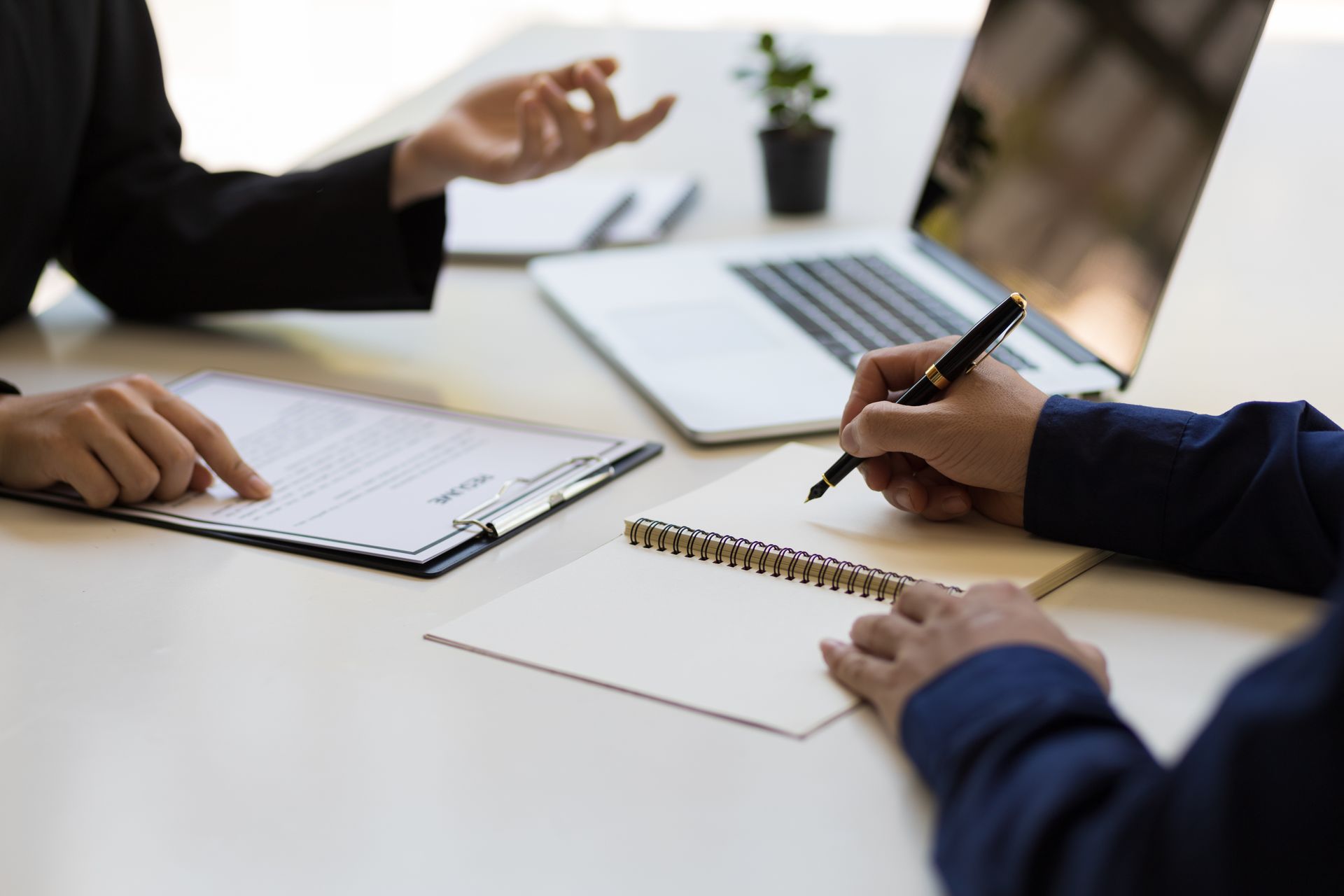 Zwei Personen an einem Schreibtisch, eine zeigt auf ein Dokument, die andere macht sich Notizen in einem Spiralblock.