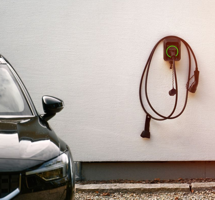 Schwarzes Elektroauto neben einer weißen Wand mit montierter Ladestation.