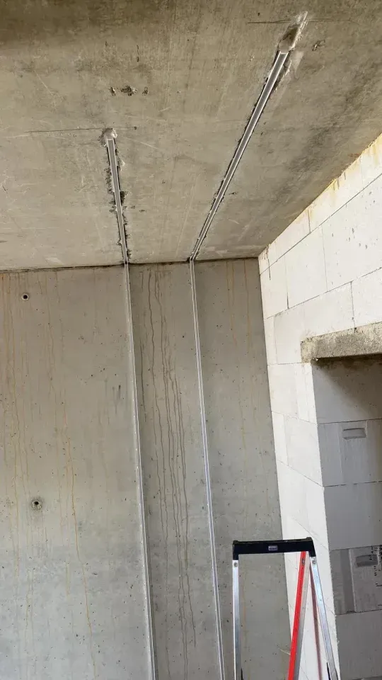 Betondecke und -wand mit sichtbarer Stahlbewehrung in einem im Bau befindlichen Gebäude. Leiter in der Ecke.