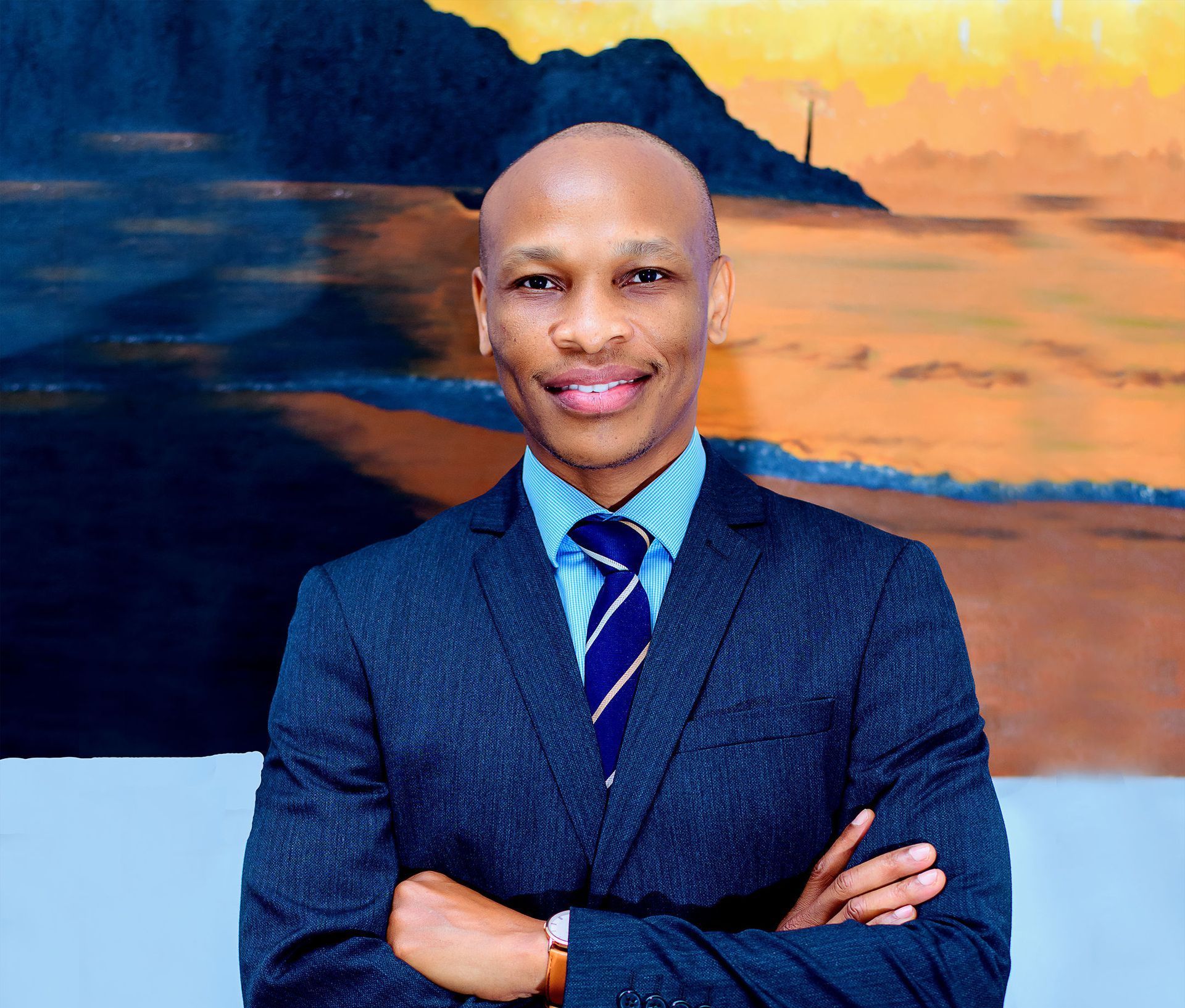 A man in a suit and tie is standing with his arms crossed in front of a painting.