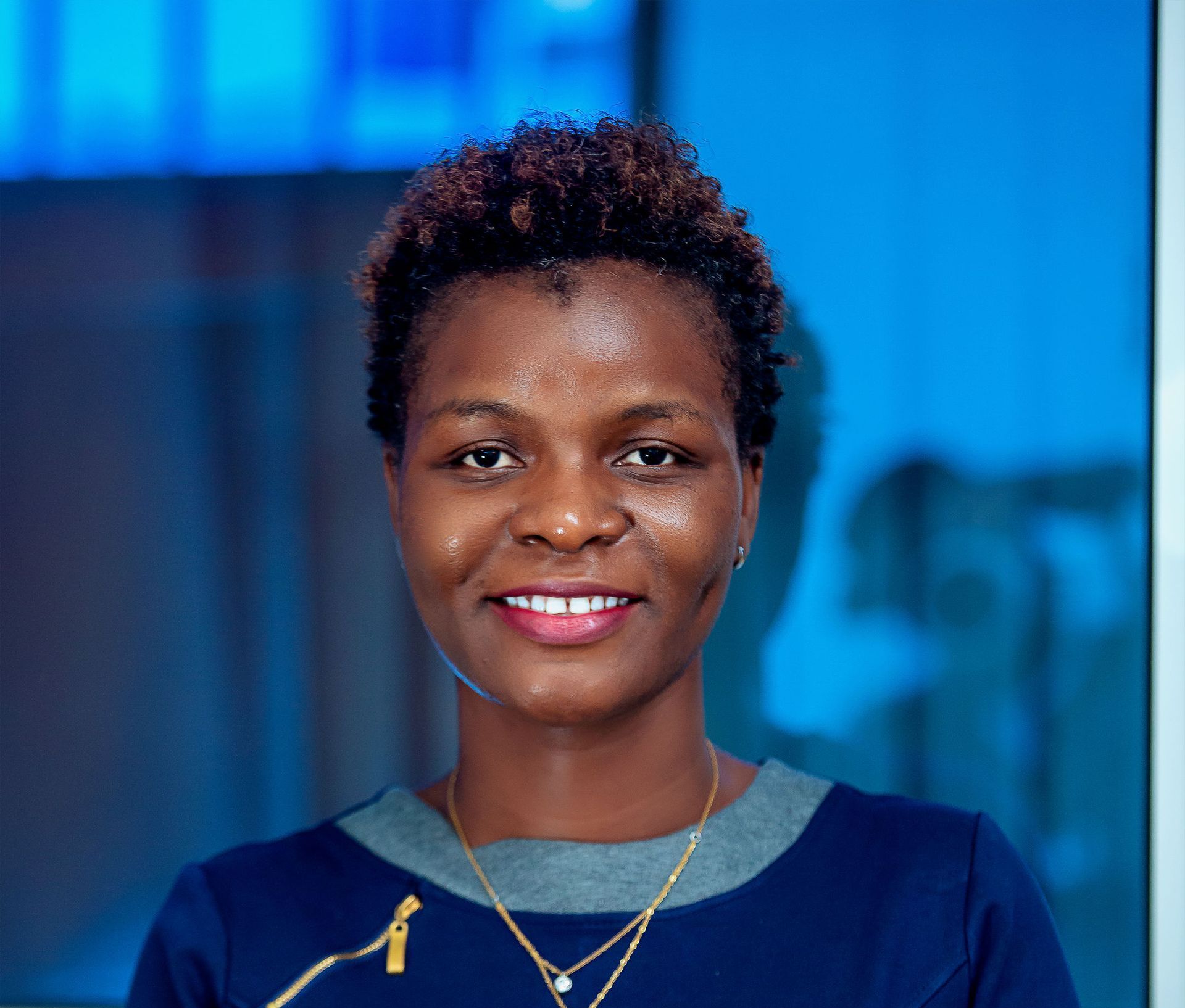 A woman wearing a blue shirt and a gold necklace is smiling for the camera.