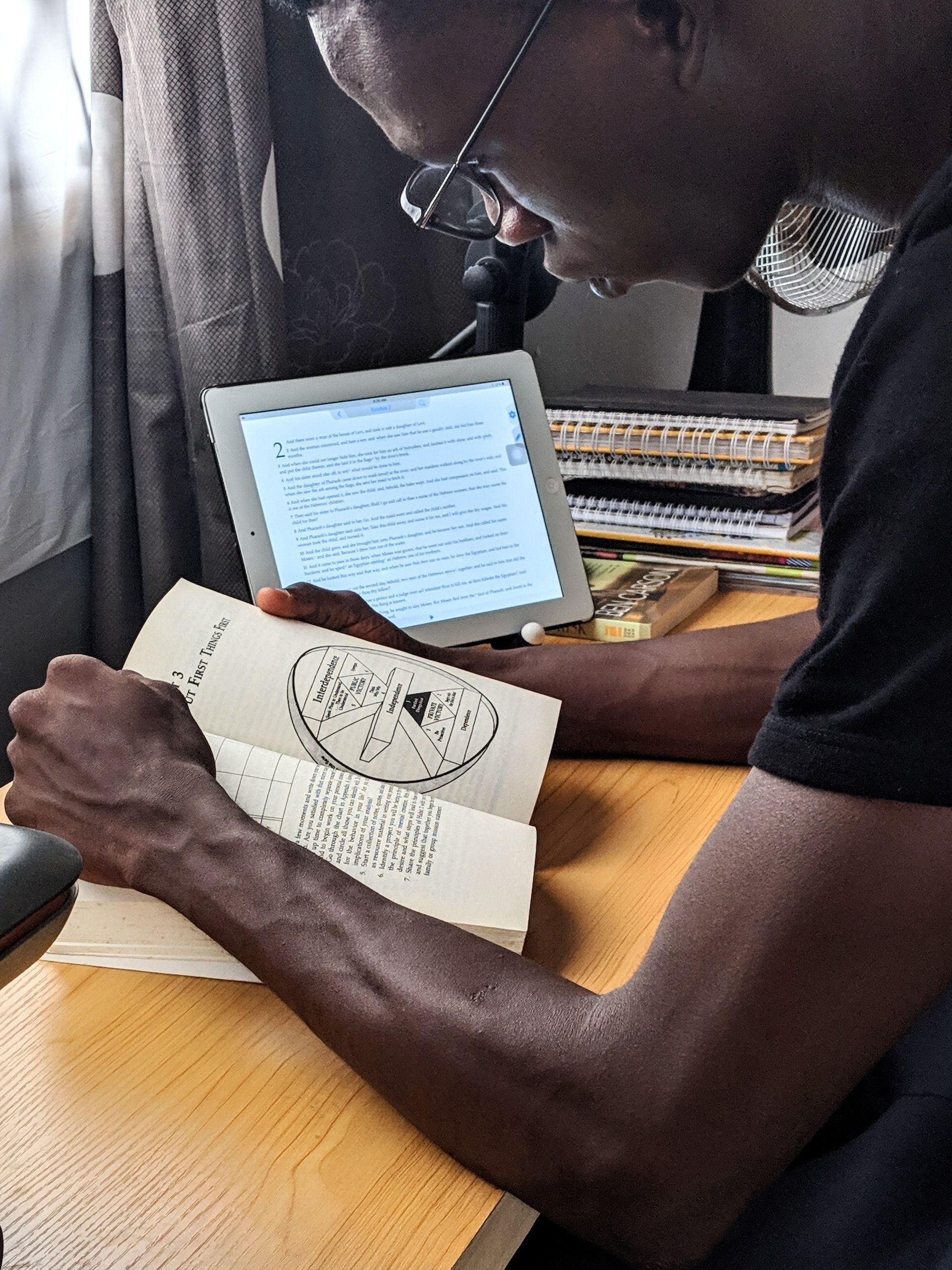 A man is reading a book while holding a tablet