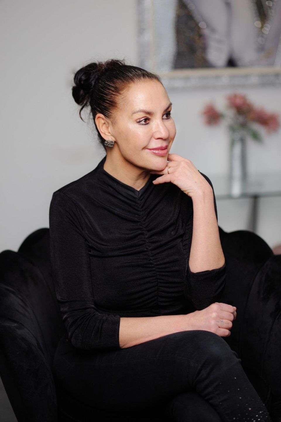 Eine Frau sitzt in einem schwarzen Stuhl und hat die Hand am Kinn.