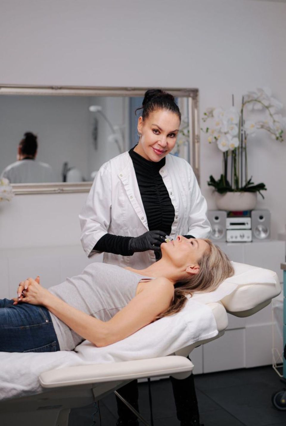 Eine Frau liegt auf einem Bett und bekommt von einem Arzt eine Gesichtsbehandlung.