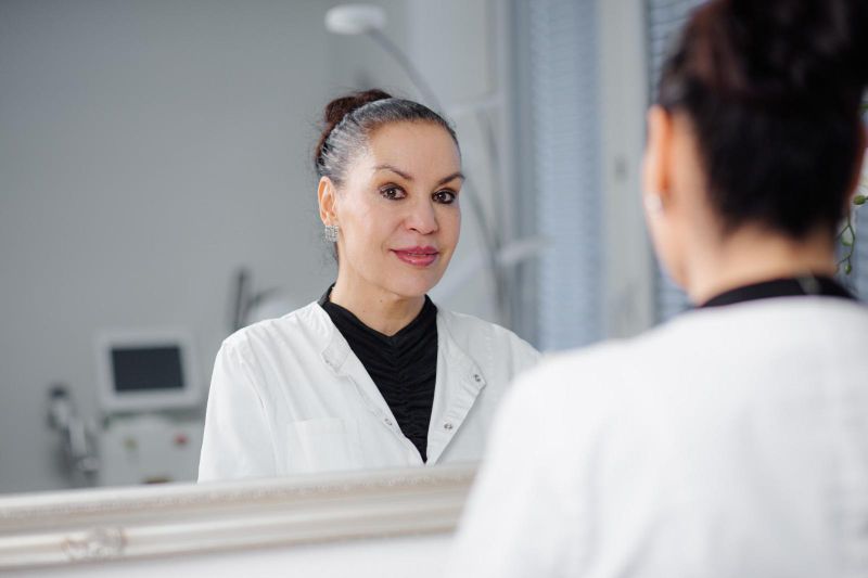 Eine Frau im Laborkittel betrachtet sich im Spiegel.