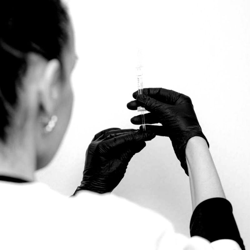 Eine Frau mit schwarzen Handschuhen hält eine Spritze