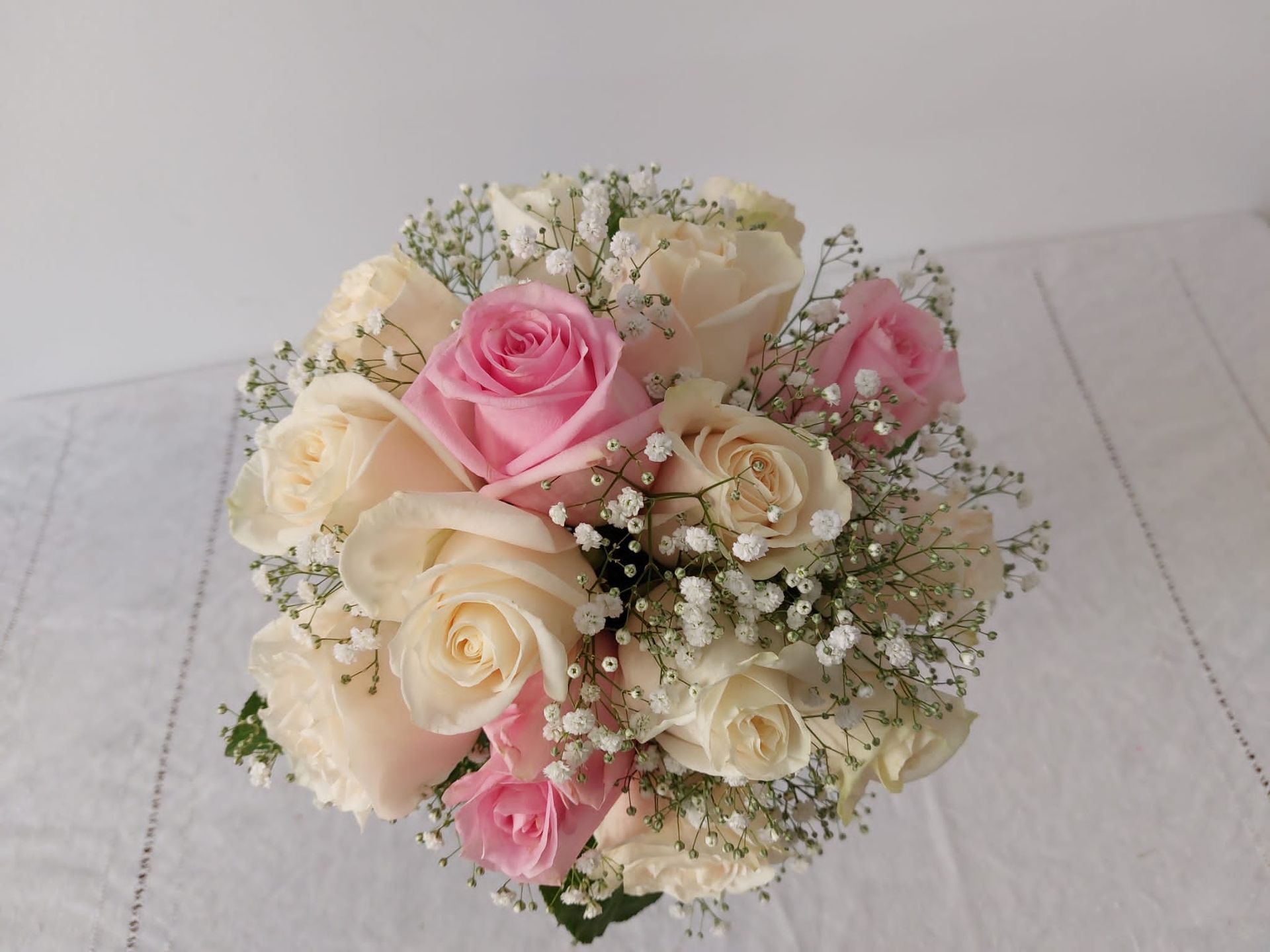 Primer plano de un ramo de rosas blancas y rosadas con aliento de bebé, dispuesto sobre un mantel blanco.