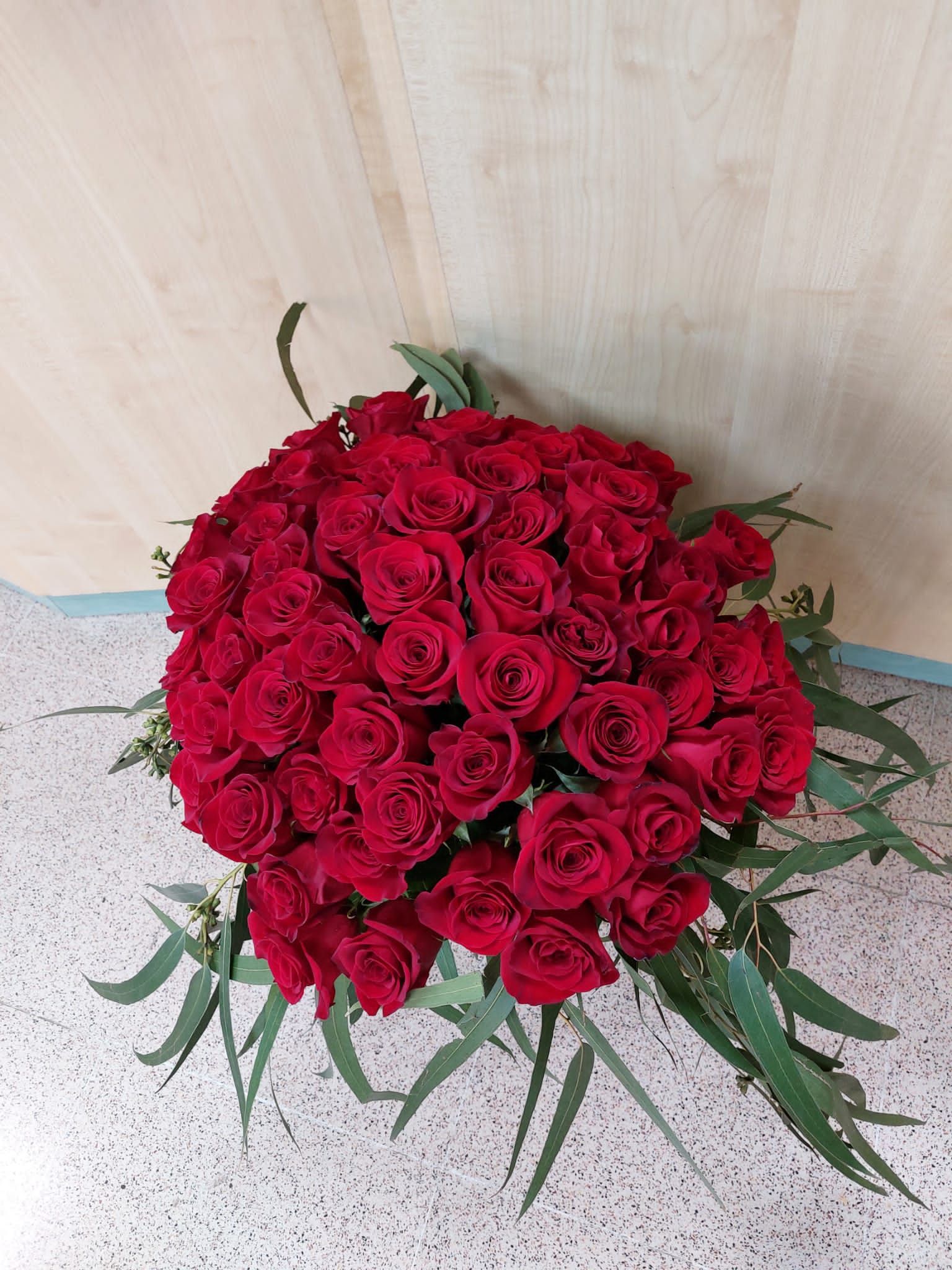 Ramo de rosas rojas y follaje verde sobre una superficie estampada, sobre un fondo de madera clara.