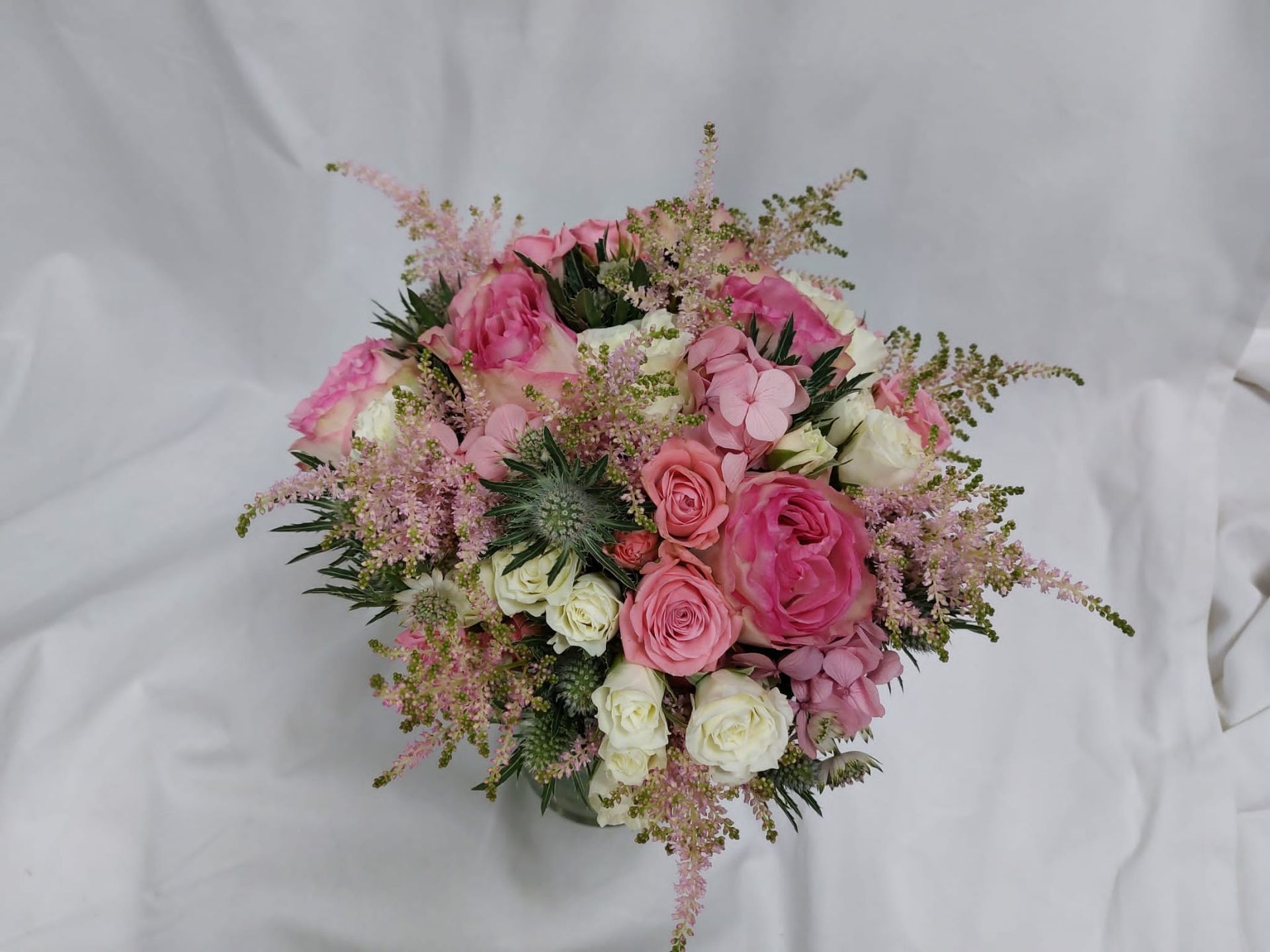 Un ramo redondo de rosas rosadas y blancas, con detalles rosas y vegetación, sobre un fondo blanco.