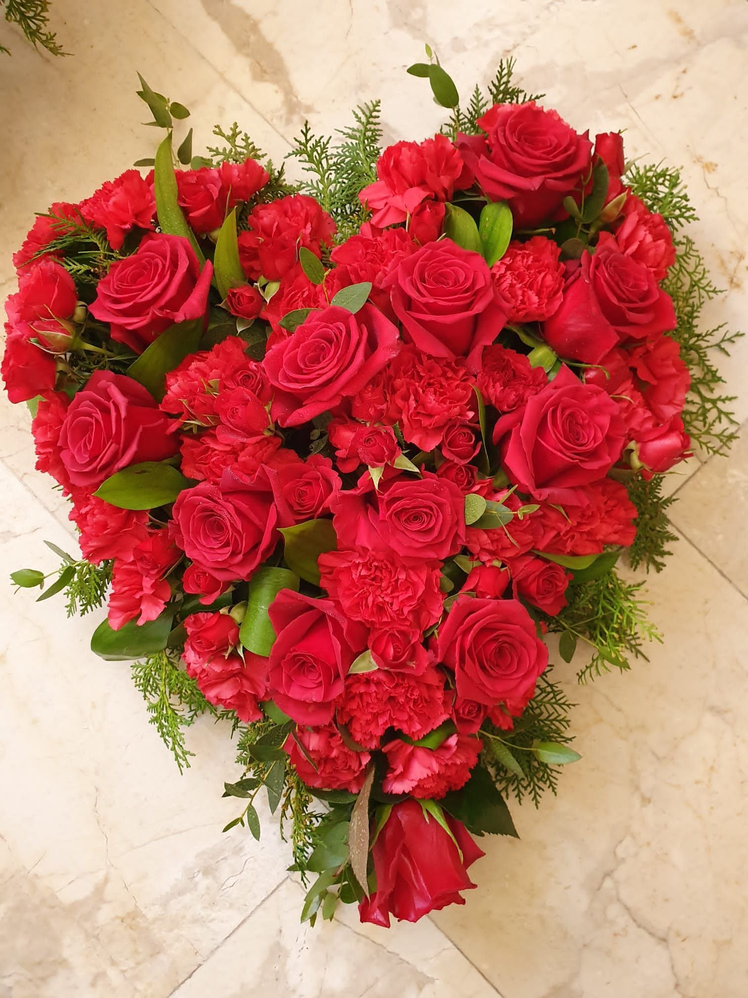 Un arreglo en forma de corazón de rosas rojas y claveles.