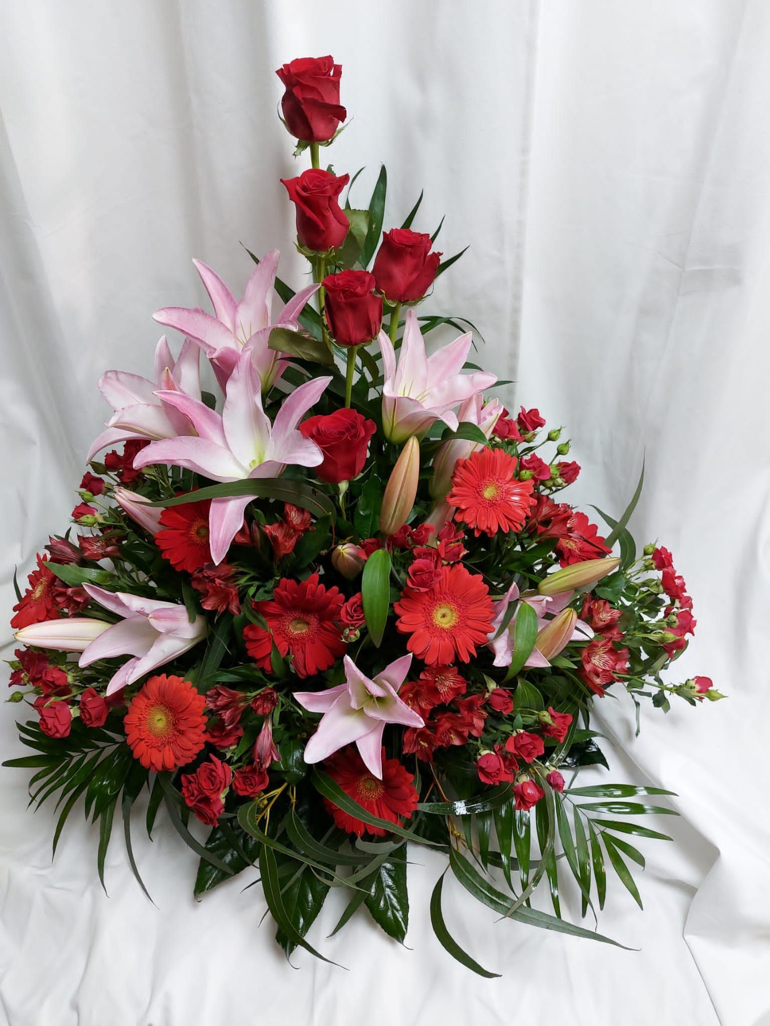 Arreglo floral rojo y rosa con rosas y lirios sobre fondo blanco.