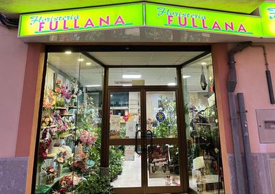 Exterior de la floristería Fullana, con letrero verde sobre la puerta de cristal de la entrada. Se ven flores y plantas en el interior.
