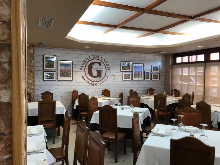 Comedor de restaurante con manteles blancos, sillas de madera, pared de ladrillo y fotos.