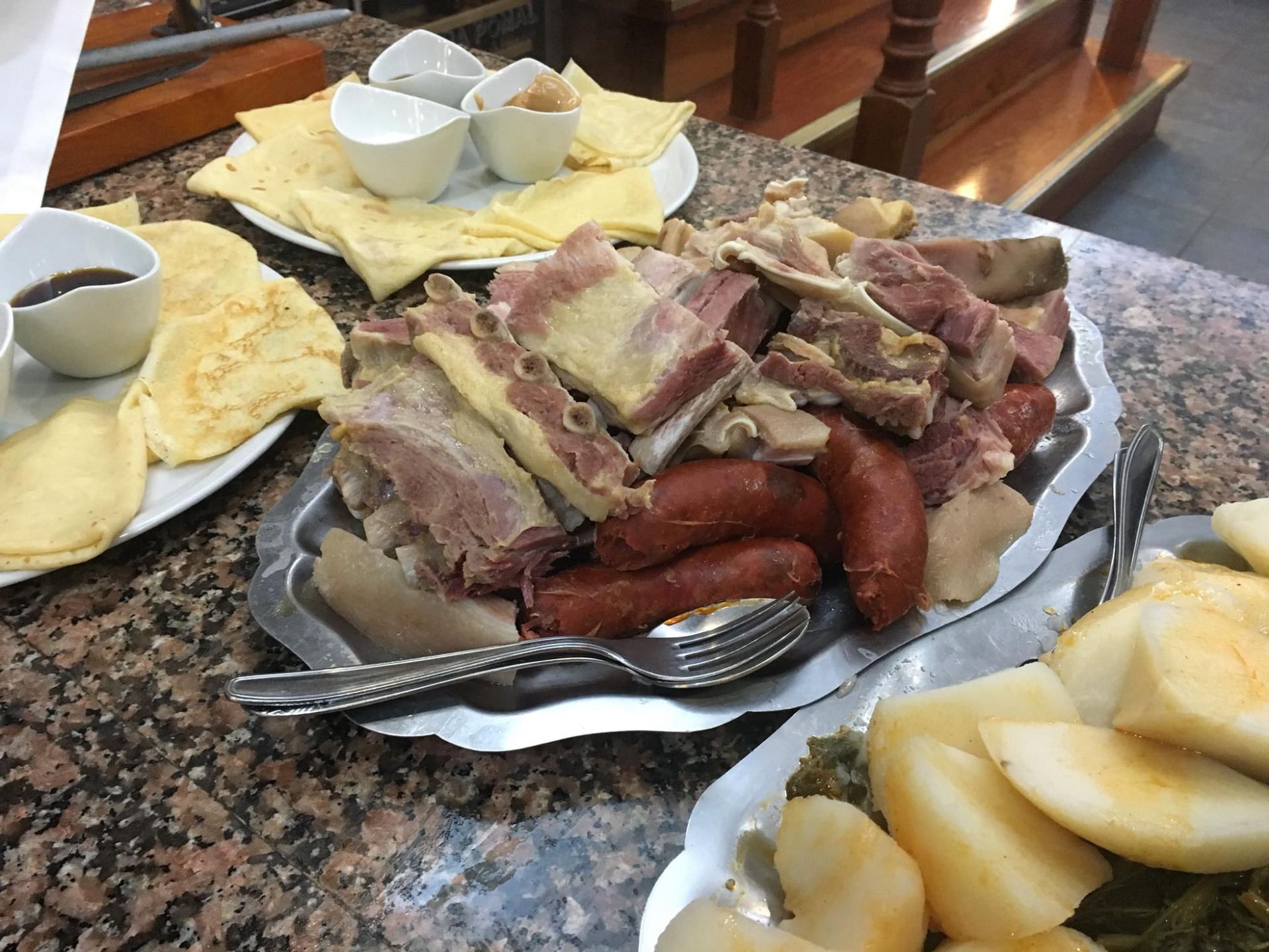 Carnes variadas y embutidos con crepes, patatas y salsas en una mesa de un restaurante.