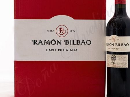 Caja y botella de vino tinto y blanco Ramón Bilbao; vino tinto oscuro con etiqueta blanca.