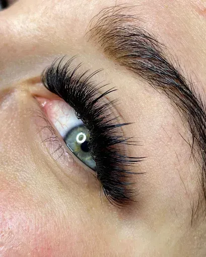 Primer plano de un ojo con largas extensiones de pestañas oscuras y una ceja perfilada.