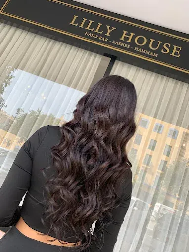 Mujer con cabello largo, oscuro y ondulado, de pie frente a las cortinas del escaparate de la tienda Lilly House.