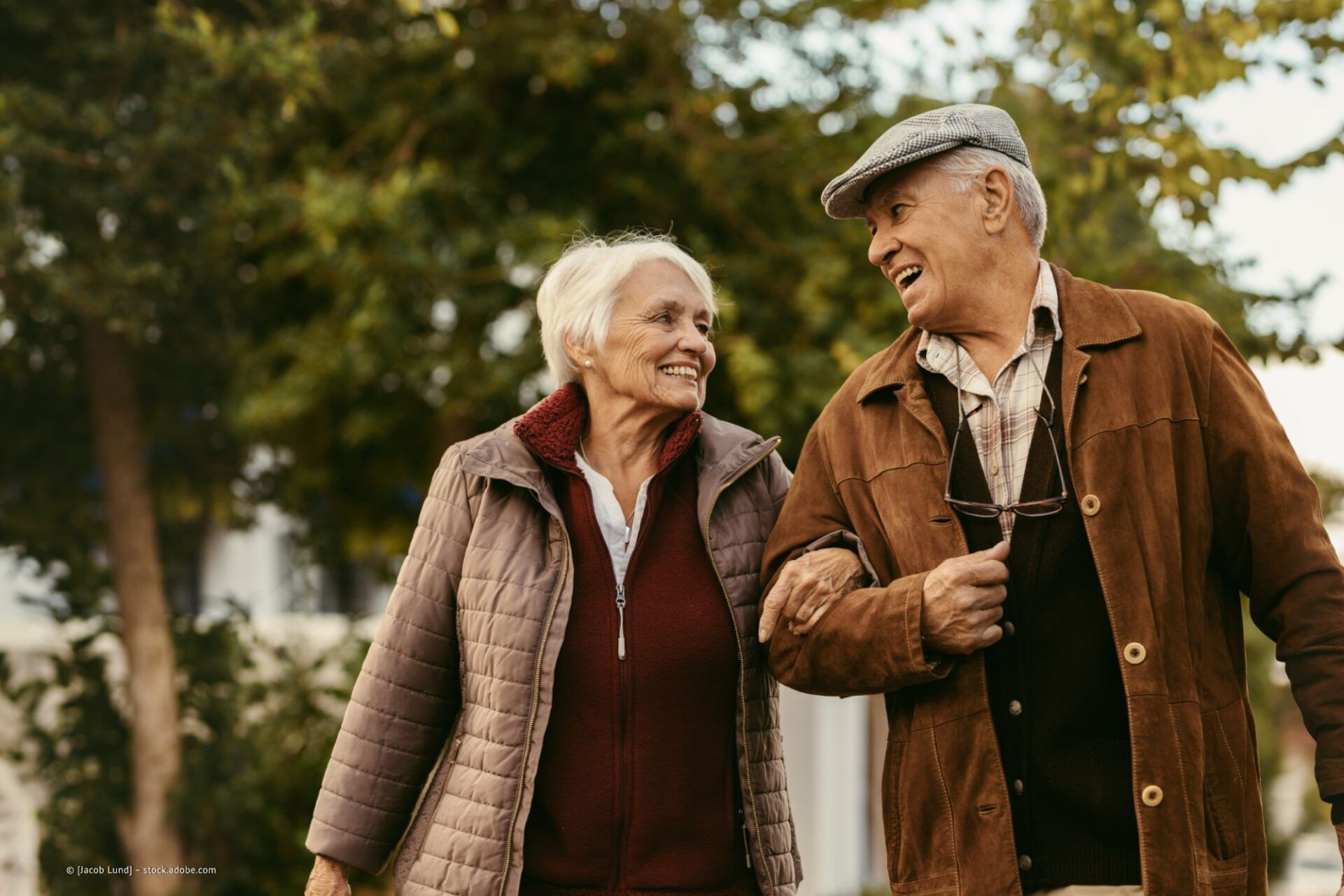Altes Ehepaar geht eingehakt und lächelt sich an