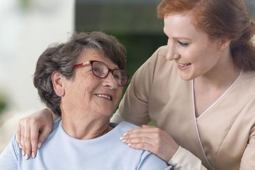 Junge Frau hält ältere Frau an den Schultern und lächelt sie über die Schulter an