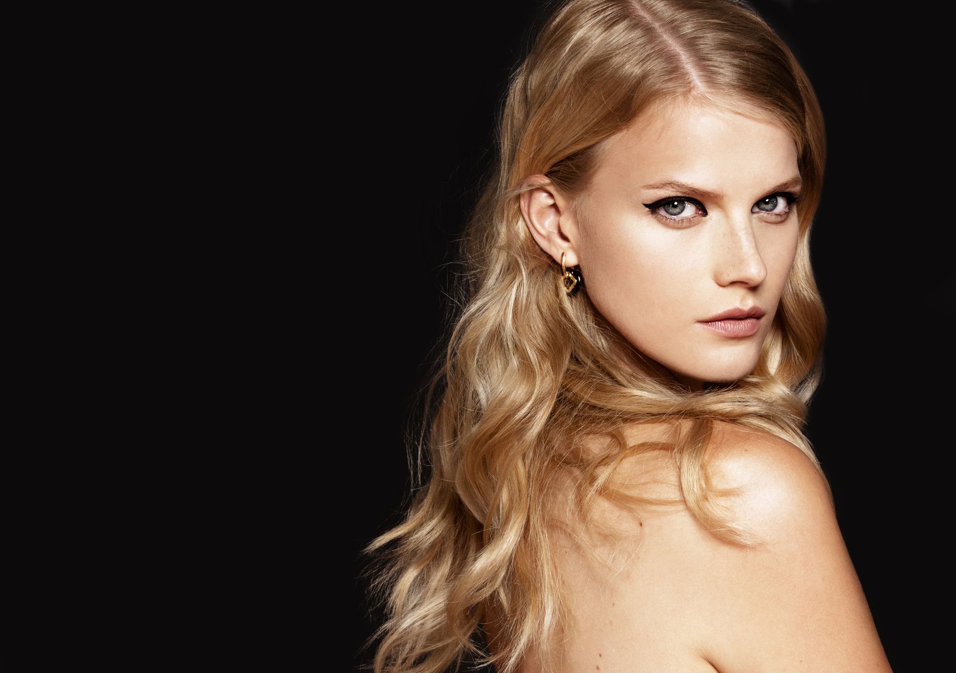 Eine Frau mit langen blonden Haaren blickt über ihre Schulter in die Kamera.