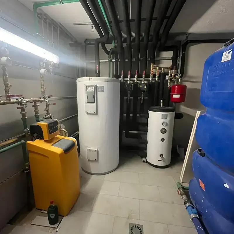 Sala de calderas con calentadores de agua blancos, tanque amarillo, tuberías y grandes tanques de almacenamiento azules.