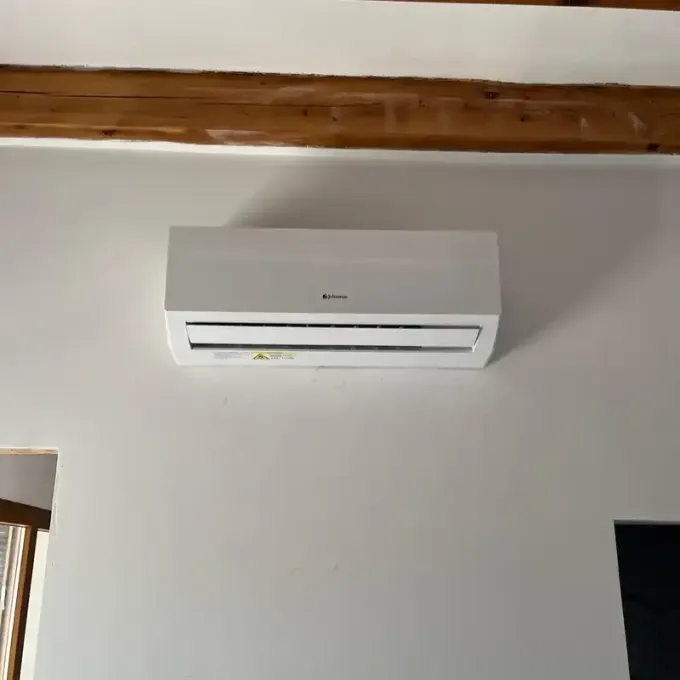 Aire acondicionado blanco montado en la pared debajo de una viga de madera en el techo.