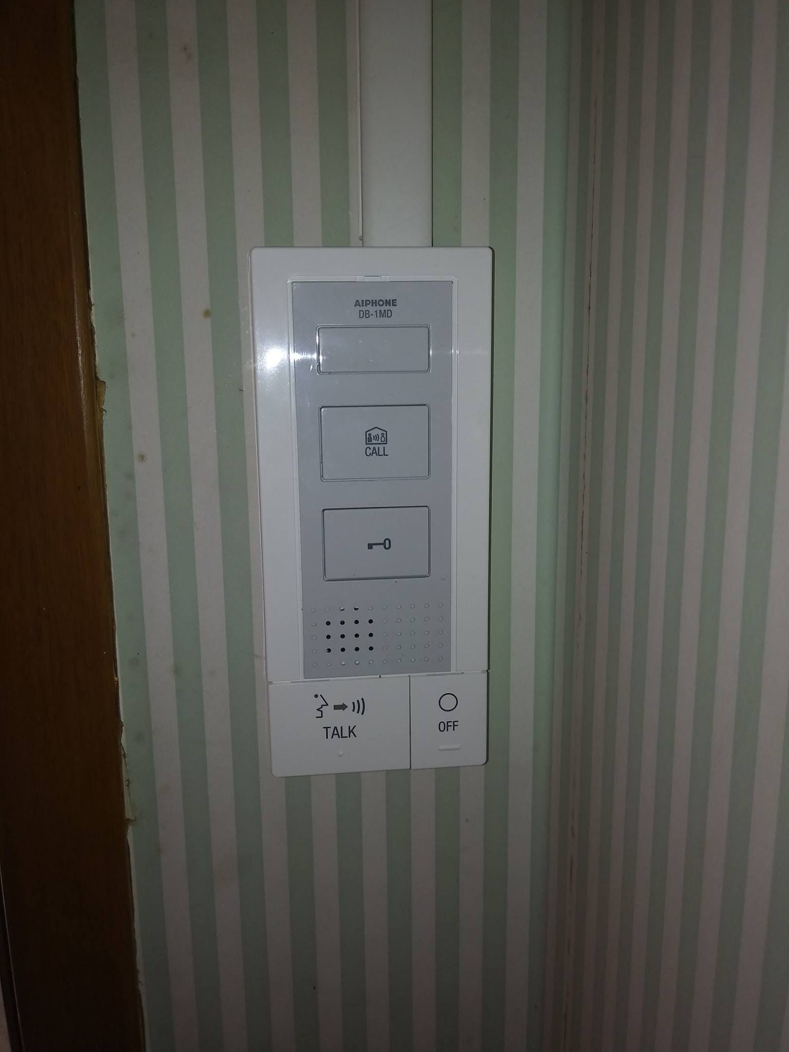 Système d'interphone blanc sur papier peint à rayures, avec boutons et prises de courant.