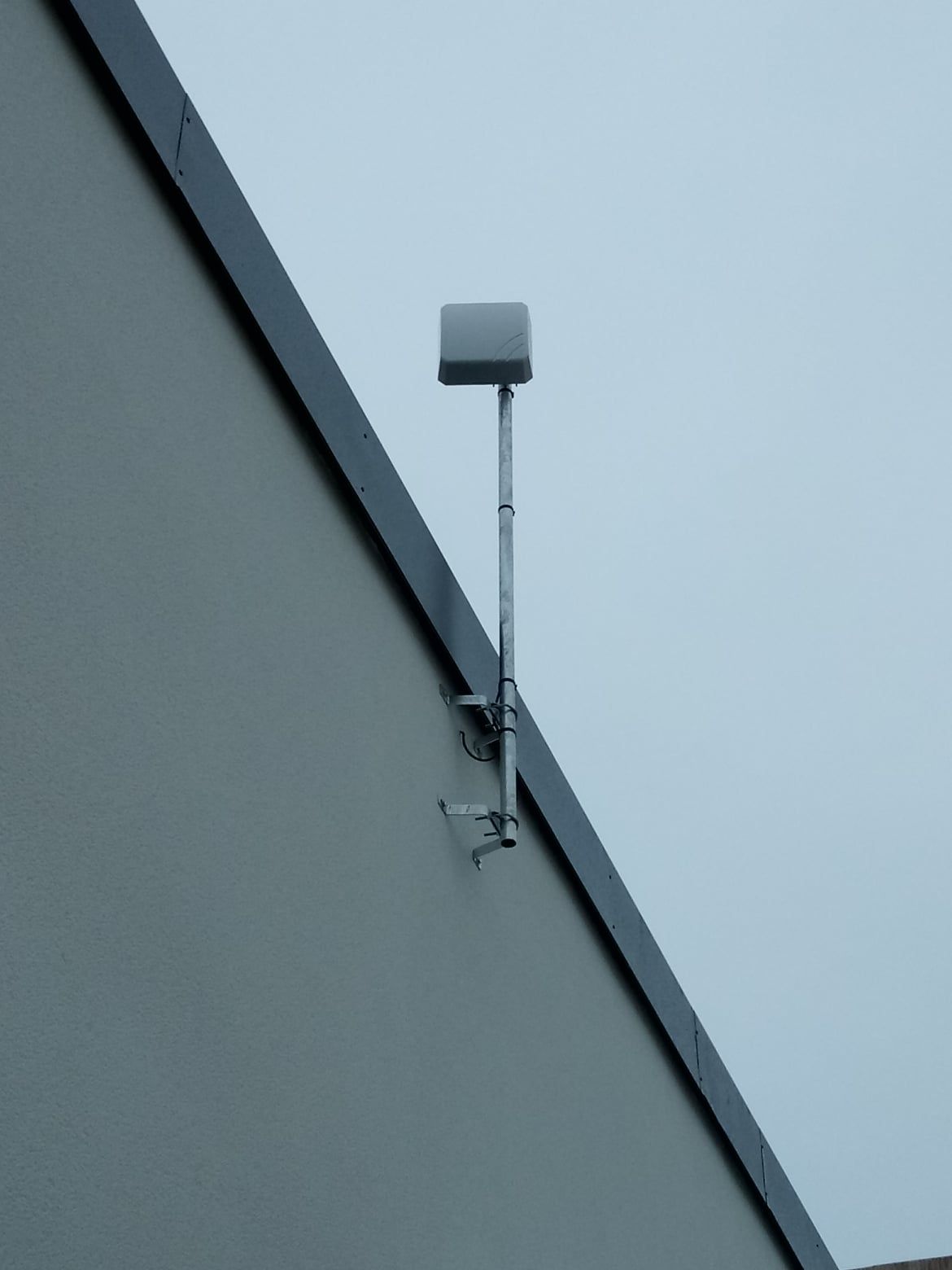 Antenne carrée montée sur un poteau, fixée à l'extérieur d'un bâtiment gris clair.