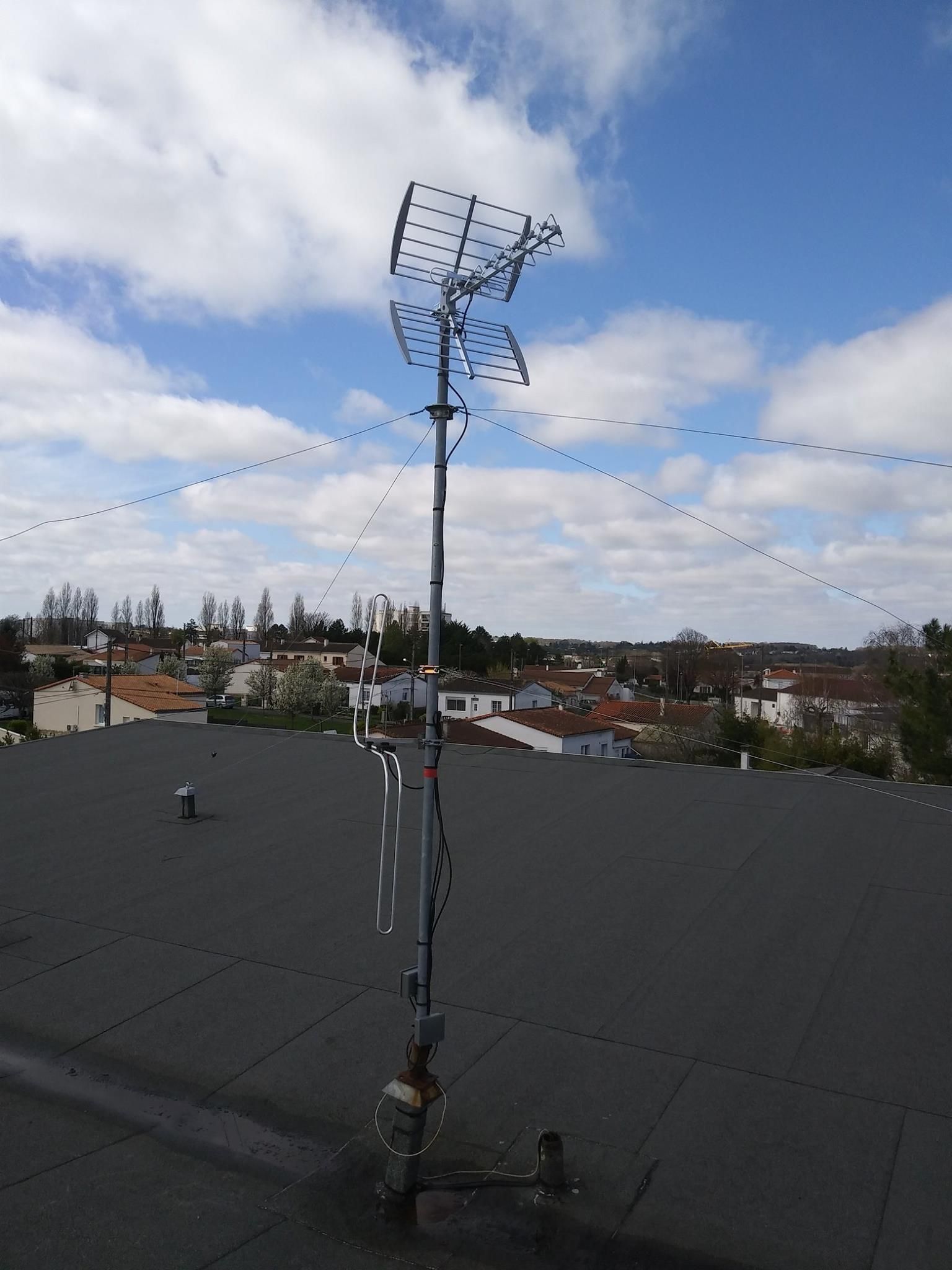 Antenne de télévision sur un toit contre un ciel nuageux, surplombant une ville.