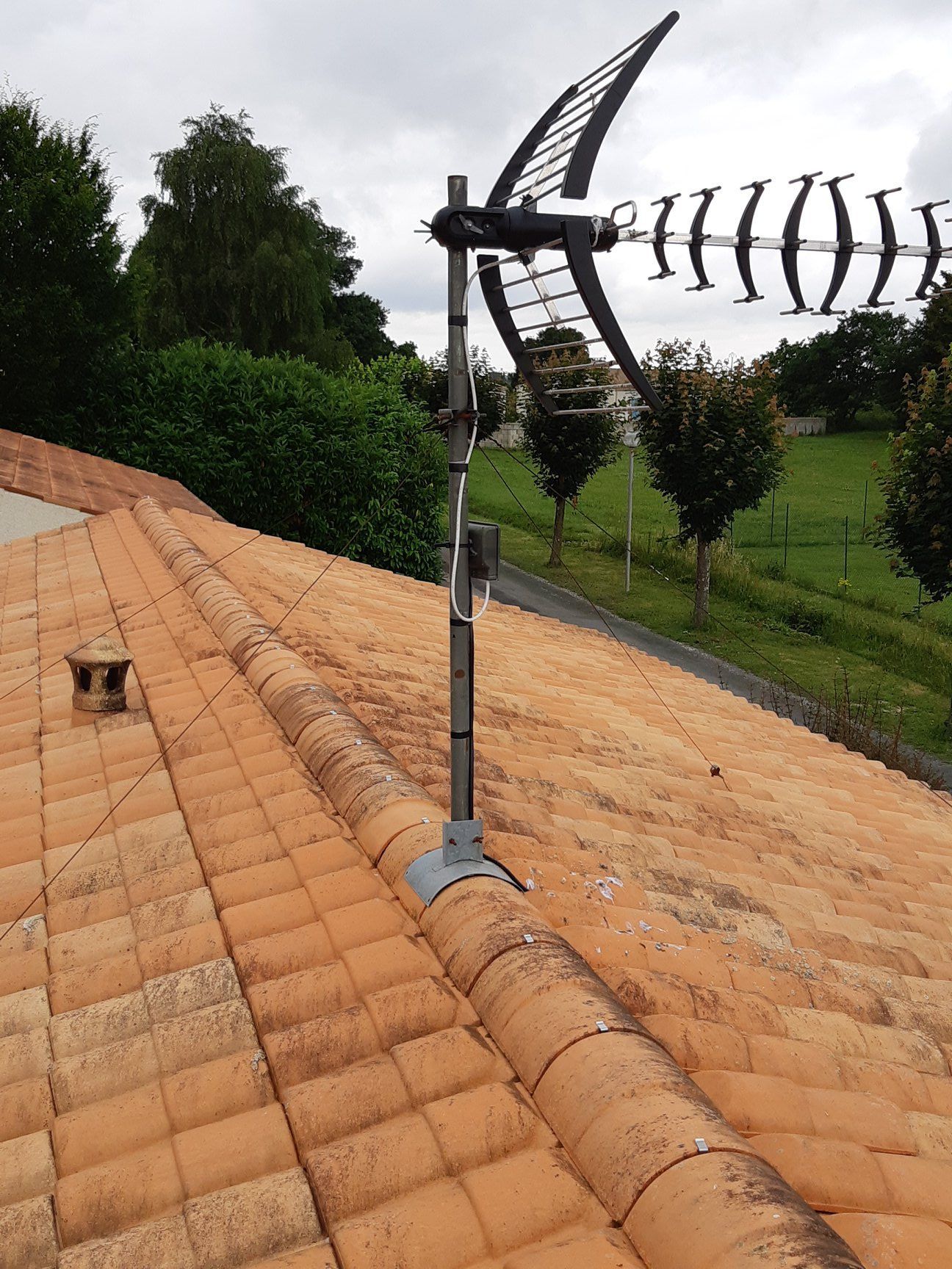 Antenne de télévision montée sur un toit de tuiles rouges avec des arbres verts en arrière-plan.