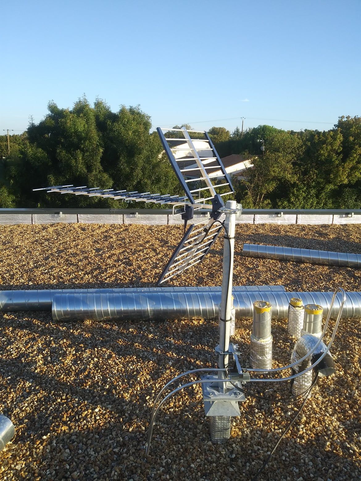 Une antenne de télévision montée sur un toit avec des arbres en arrière-plan, sous un ciel bleu clair.