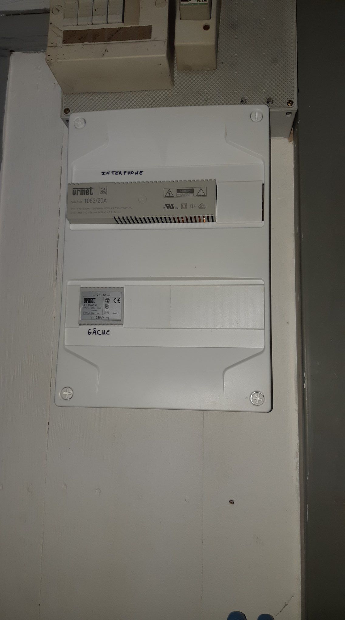 Panneau électrique blanc sur un mur blanc avec un coffret électrique en haut.