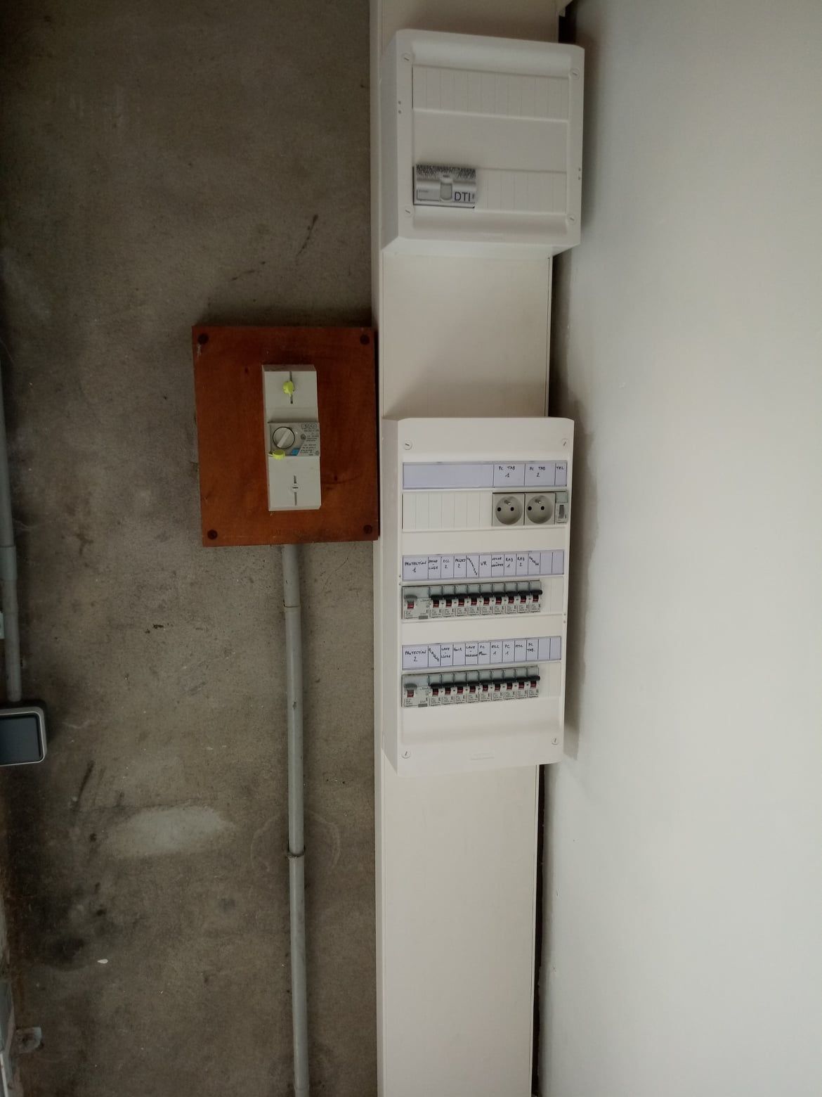 Panneaux électriques sur un mur en béton, avec conduit et un coin peint en blanc.