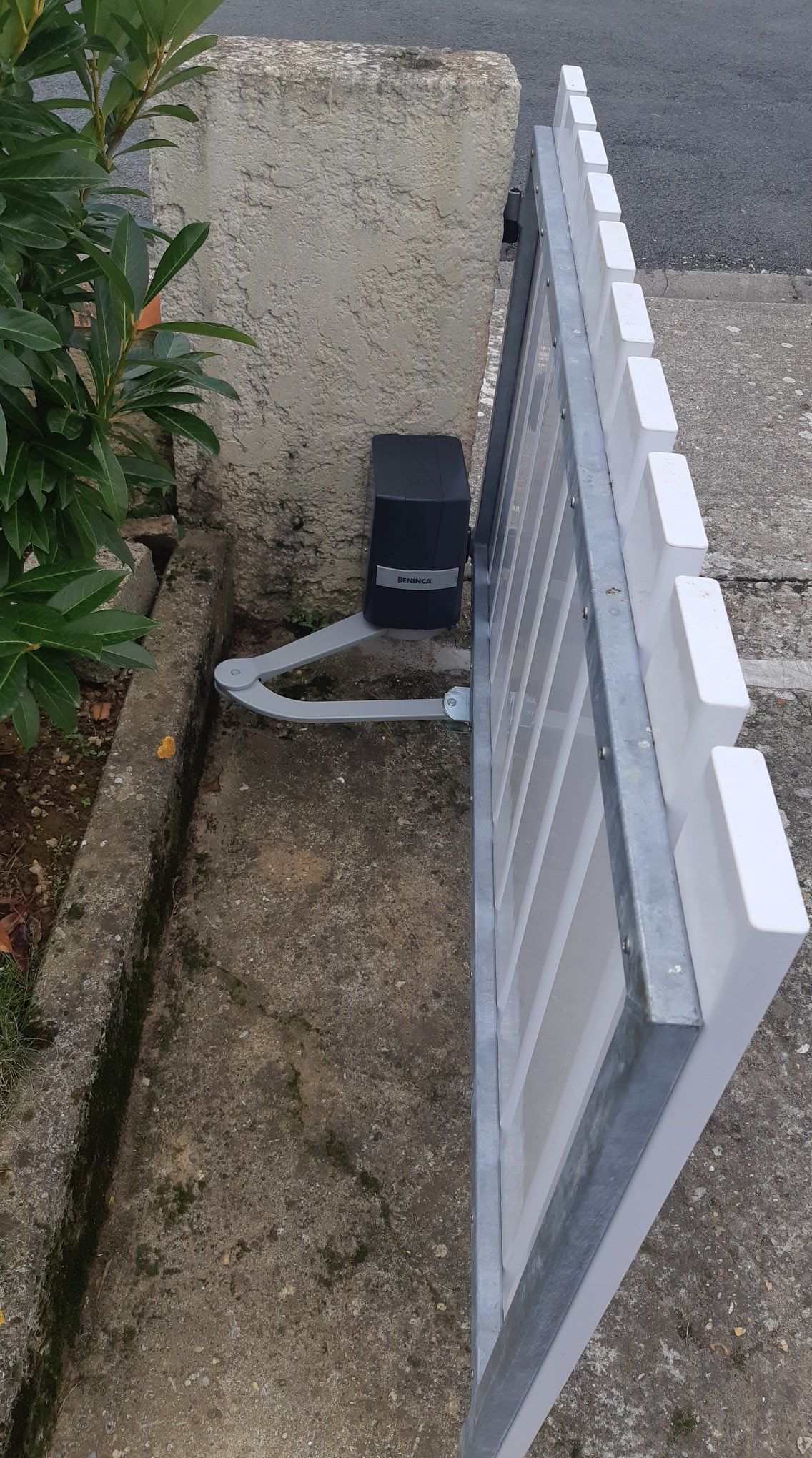 Moteur de portail automatique fixé à un portail blanc et un mur en ciment.