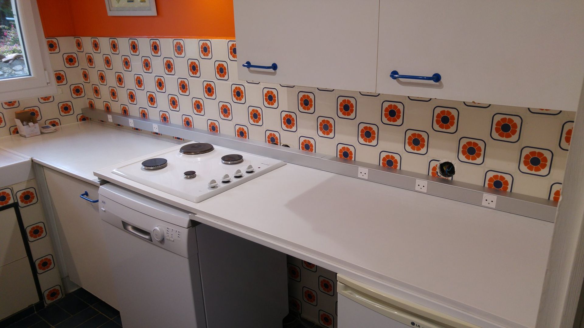 Cuisine rétro blanche et orange avec cuisinière, lave-vaisselle et dosseret à motifs.