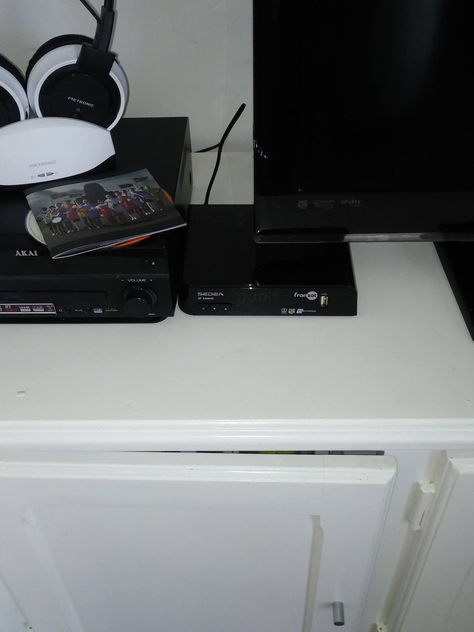 Meuble blanc avec appareils électroniques : téléviseur, lecteur DVD, décodeur, casque et une photo.