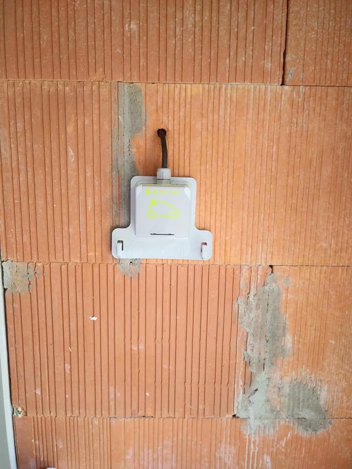 Boîte électrique grise fixée à un mur de briques rouges avec un fil exposé.