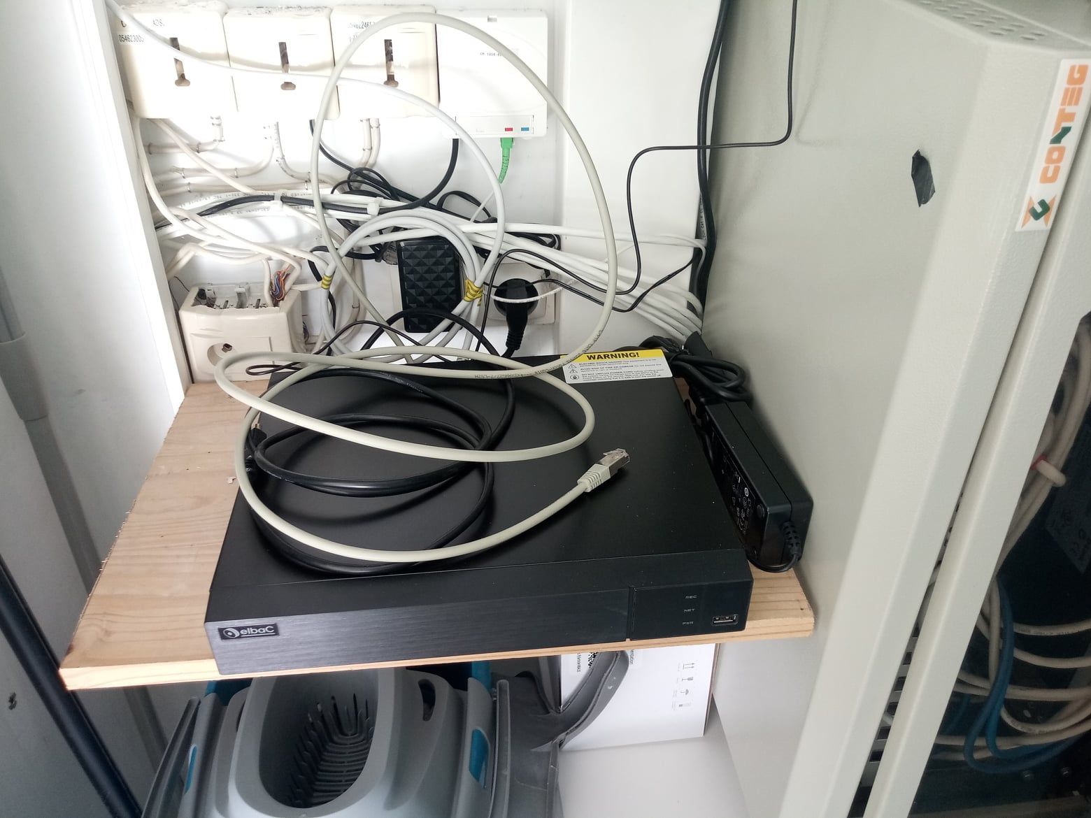 Une armoire encombrée contenant du matériel réseau : un DVR noir, des câbles et des fils.