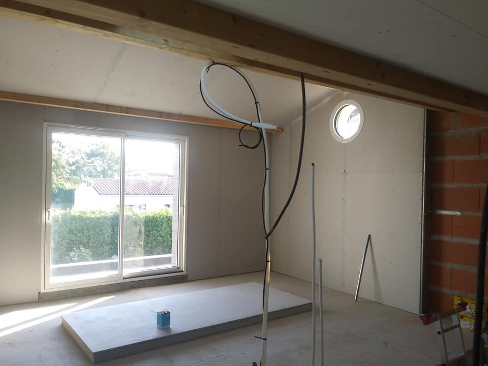 Intérieur d'une pièce en construction avec cloisons sèches, une fenêtre et des poutres apparentes.