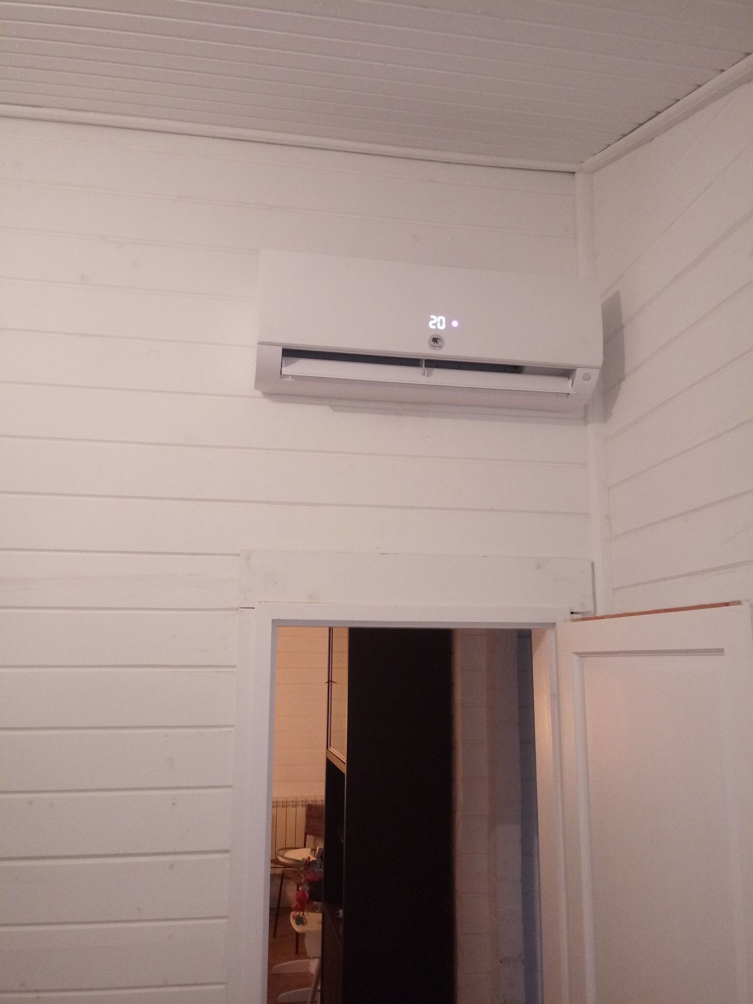 Climatiseur blanc monté sur un mur lambrissé blanc au-dessus d'une porte.