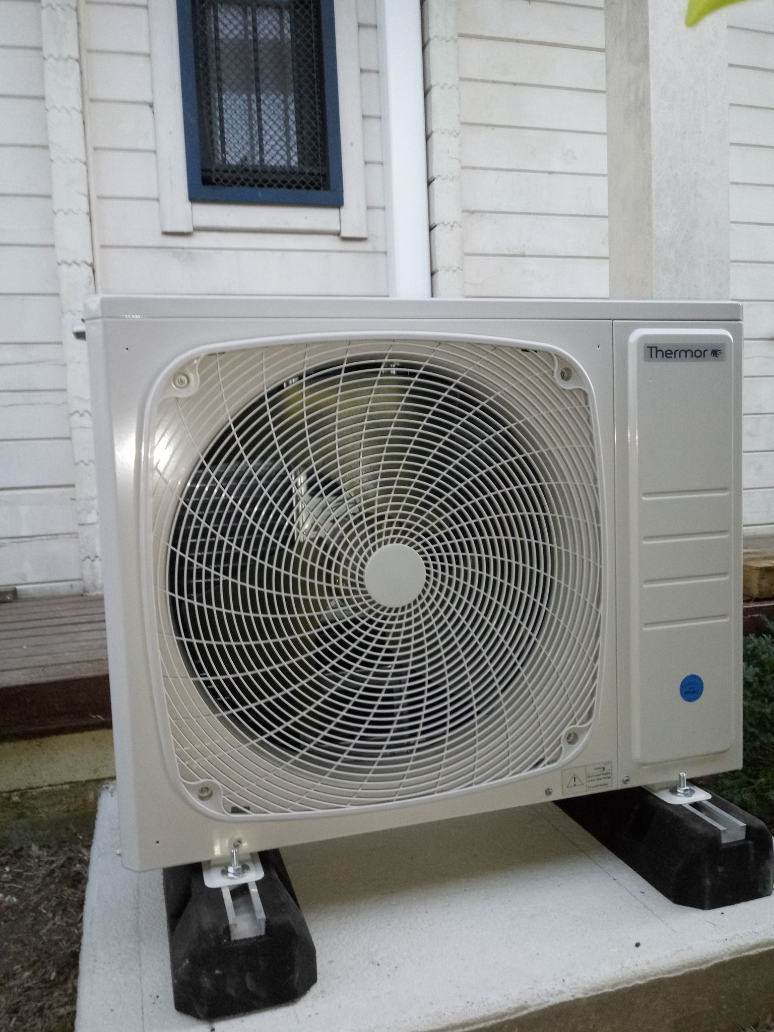 Une unité de climatisation posée sur des blocs noirs à l'extérieur d'un bâtiment blanc.