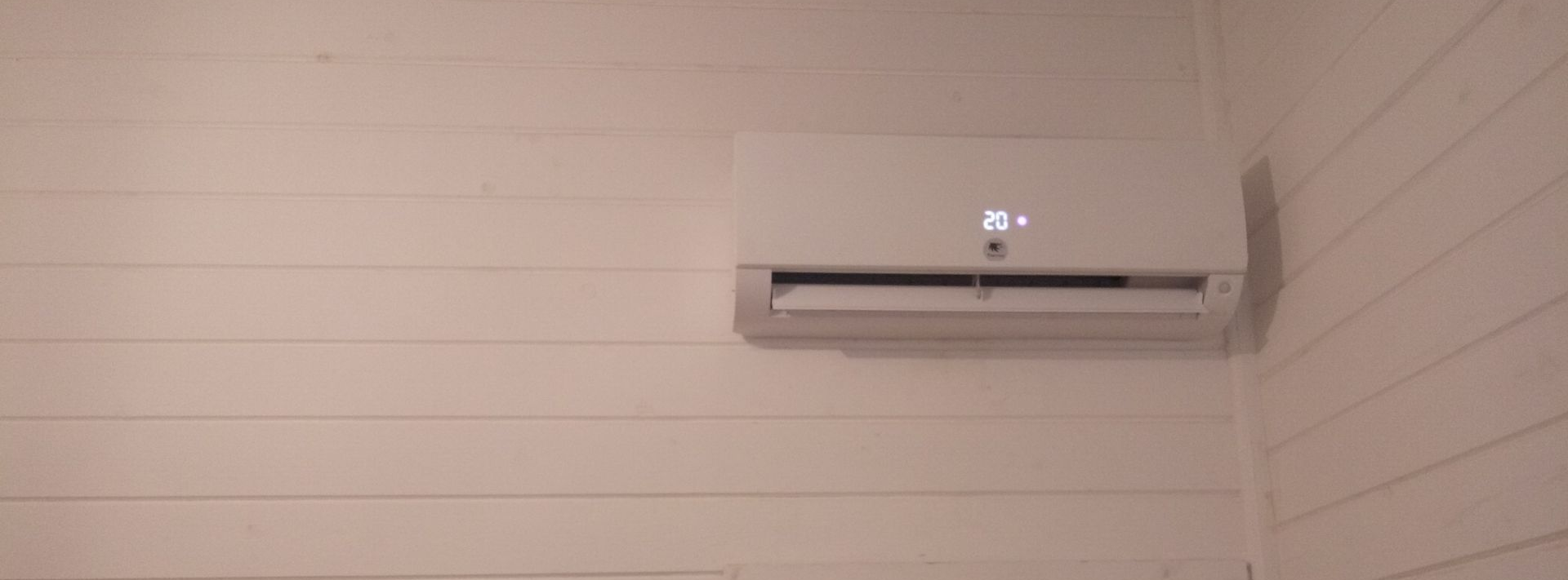 Climatiseur blanc sur un mur à clin blanc ; l'écran affiche 26.