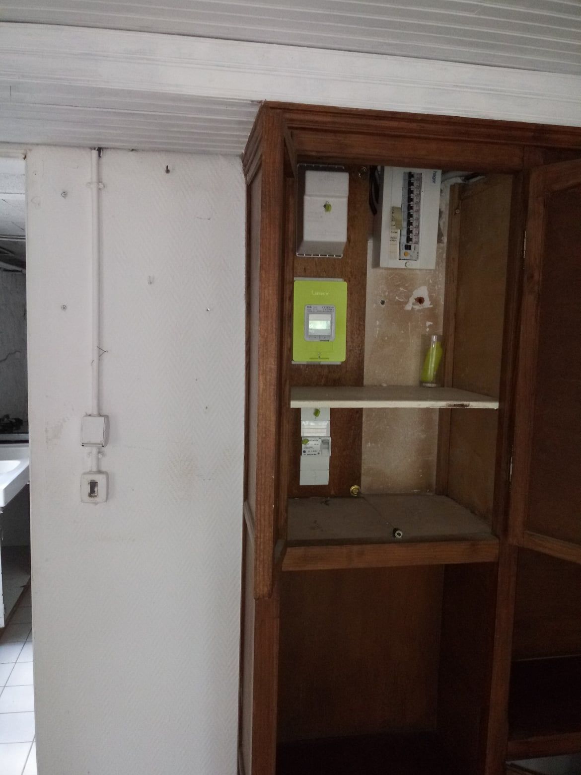 Armoire en bois abritant un panneau électrique, des compteurs et des prises, située dans un coin contre un mur blanc.